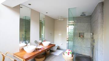 A modern bathroom with a wooden vanity, two white sinks, a large mirror, and a glass-enclosed shower area.