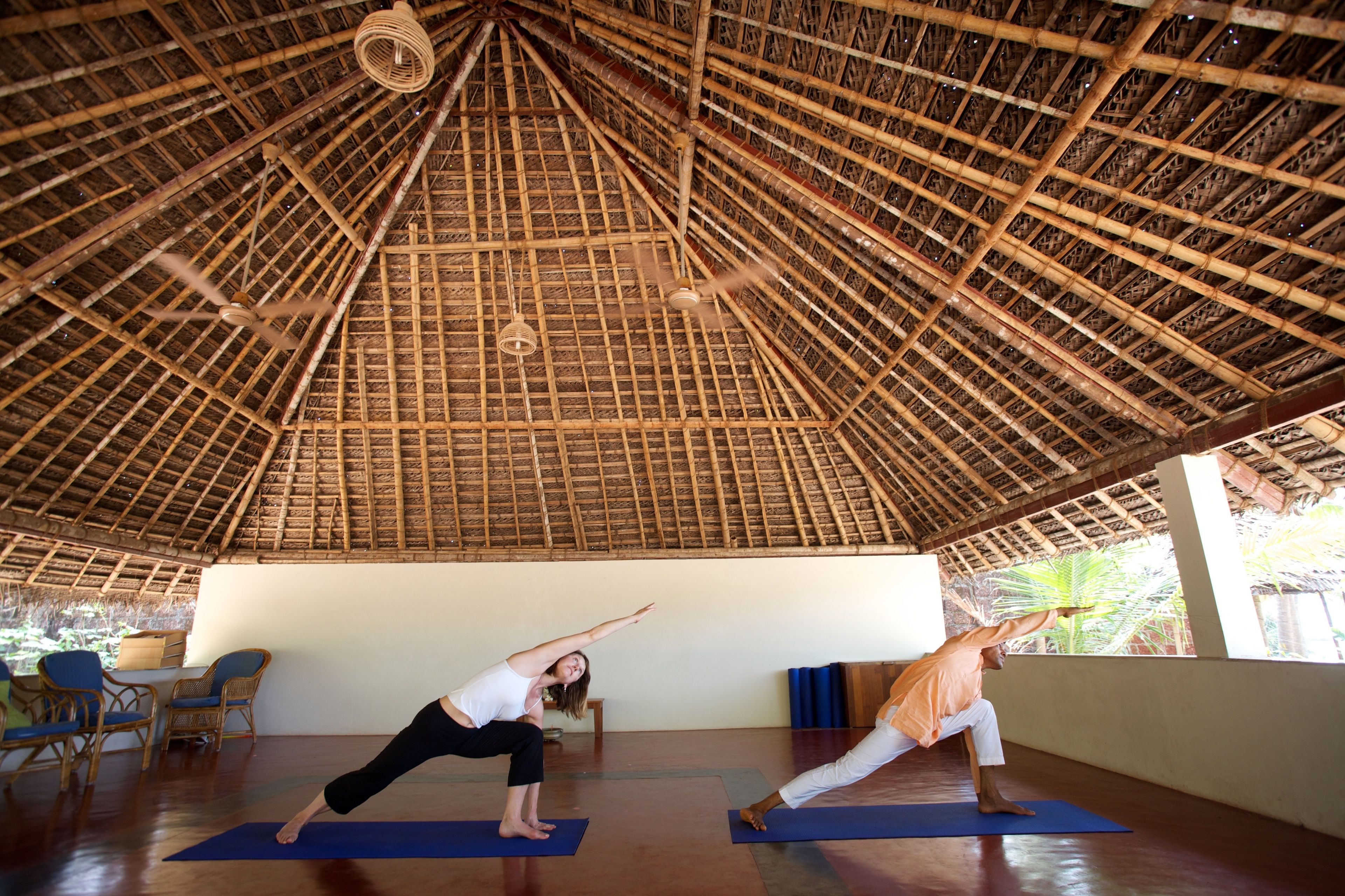 A yoga studio with a thatched roof, wooden beams, and blue mats.