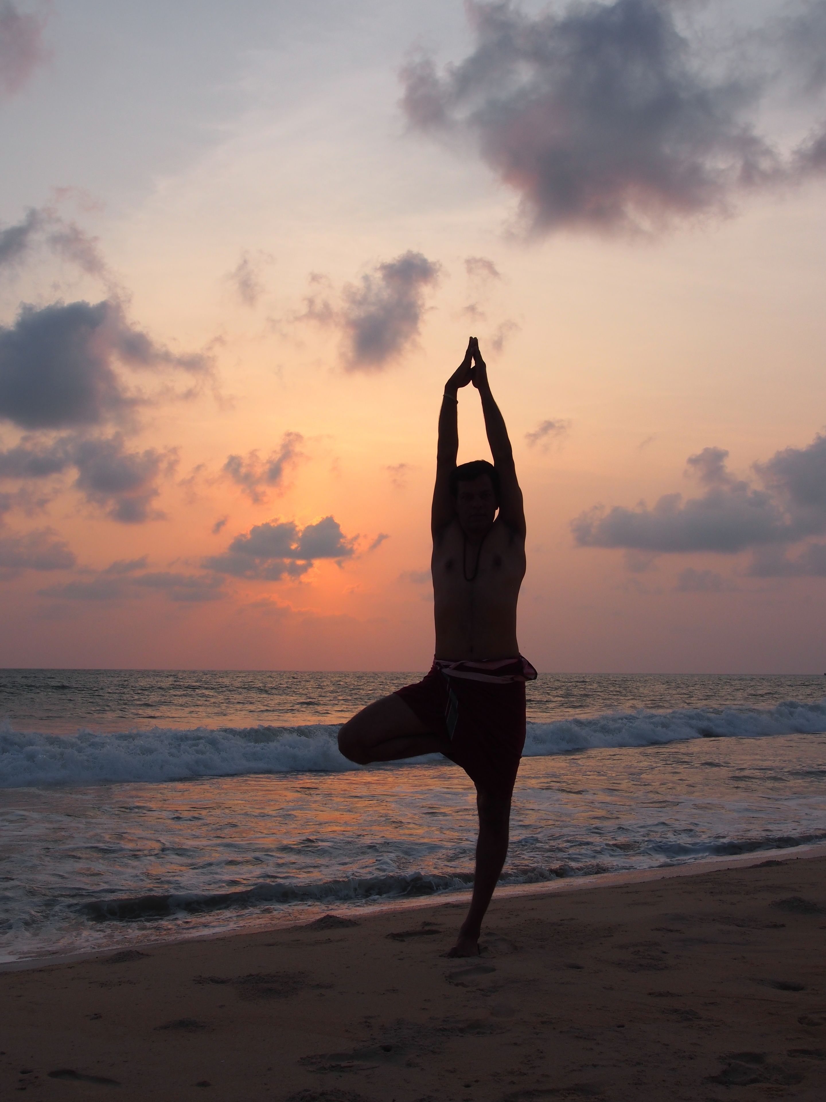 A person performing a yoga pose on a beach at sunset.