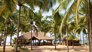 A beachside resort with thatched-roof huts, palm trees, and a sandy path. - Neeleshwar Hermitage (Hosdurg)