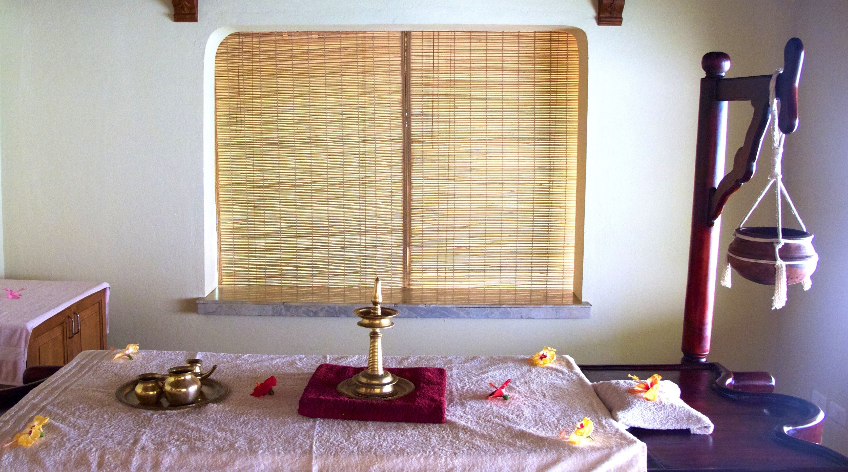 A room with a window covered by bamboo blinds, a brass oil lamp on a red cloth, and a hanging pot.