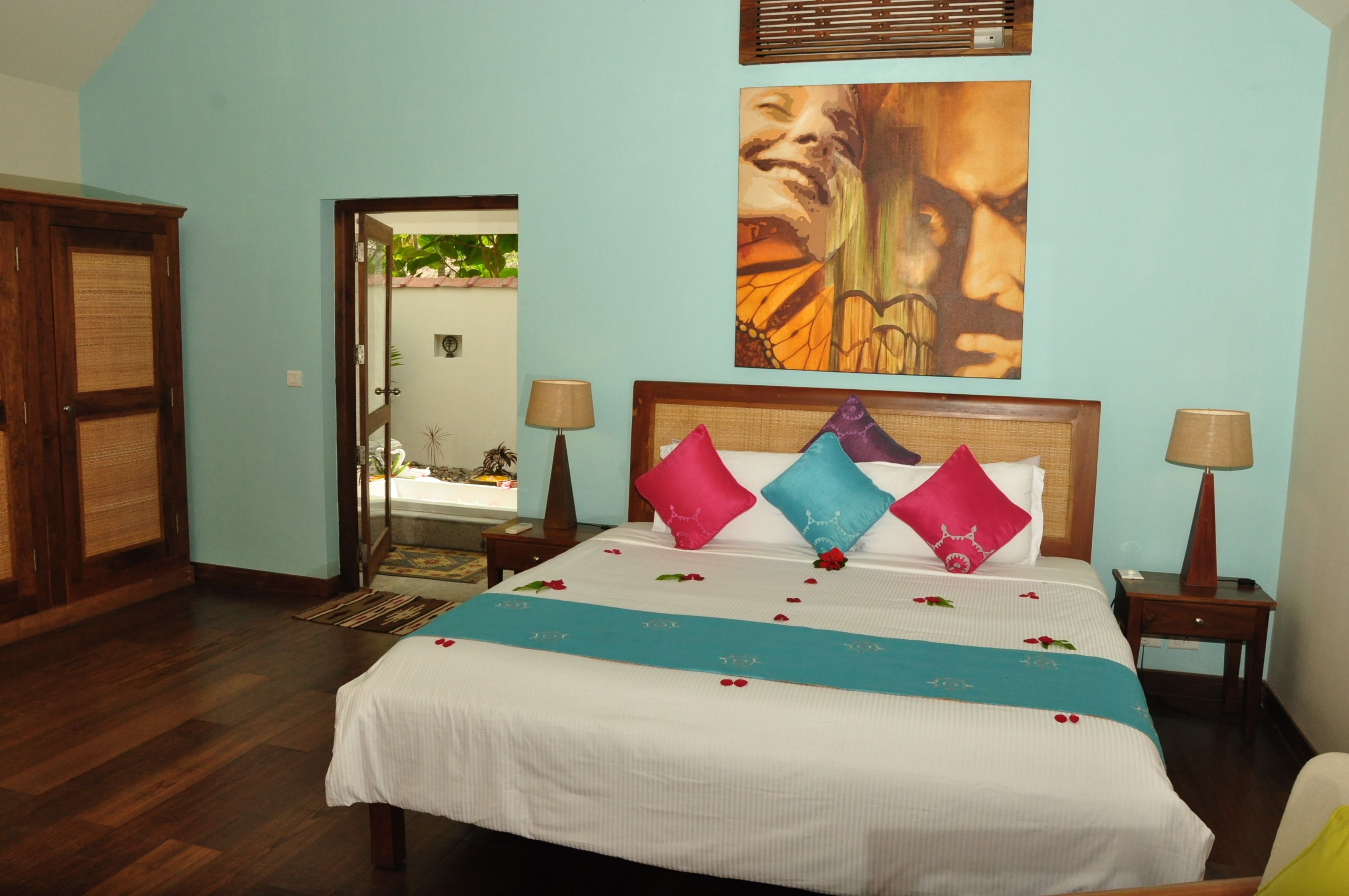 A hotel room with a bed, two bedside tables, a nightstand, a door, and a wall with a painting.