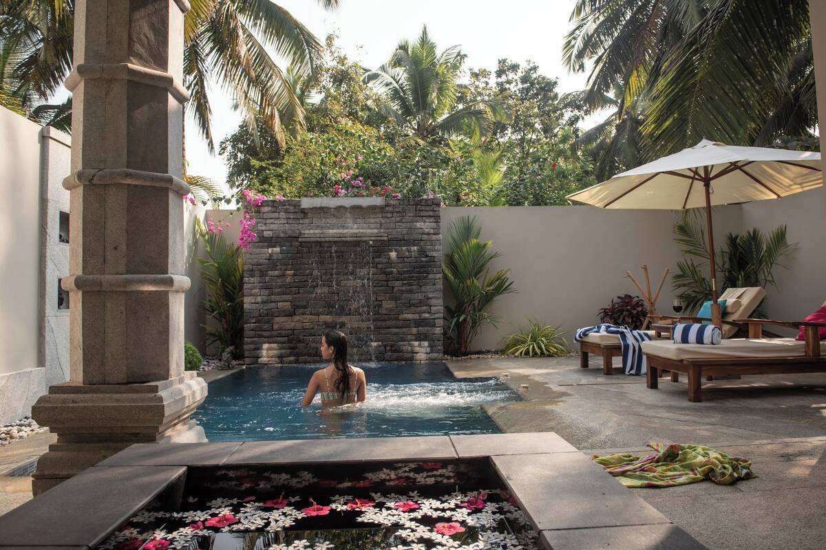 A pool area with a stone wall, lounge chairs, and an umbrella.