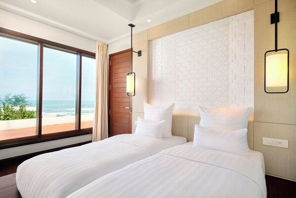 A hotel room with two beds, large windows with a view of the beach, a wooden door, and a patterned wall.