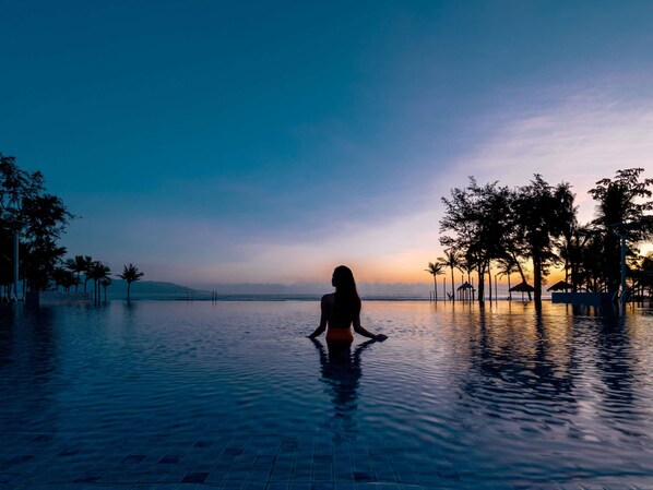 A person sitting in a pool with a sunset view.