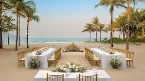 Montaje para una boda en la playa con mesas y sillas dispuestas para los invitados, palmeras y vista al océano.