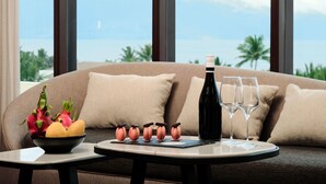 Un sofá con vistas al océano, una mesa con una botella y vasos, y un cuenco con fruta y macarons.