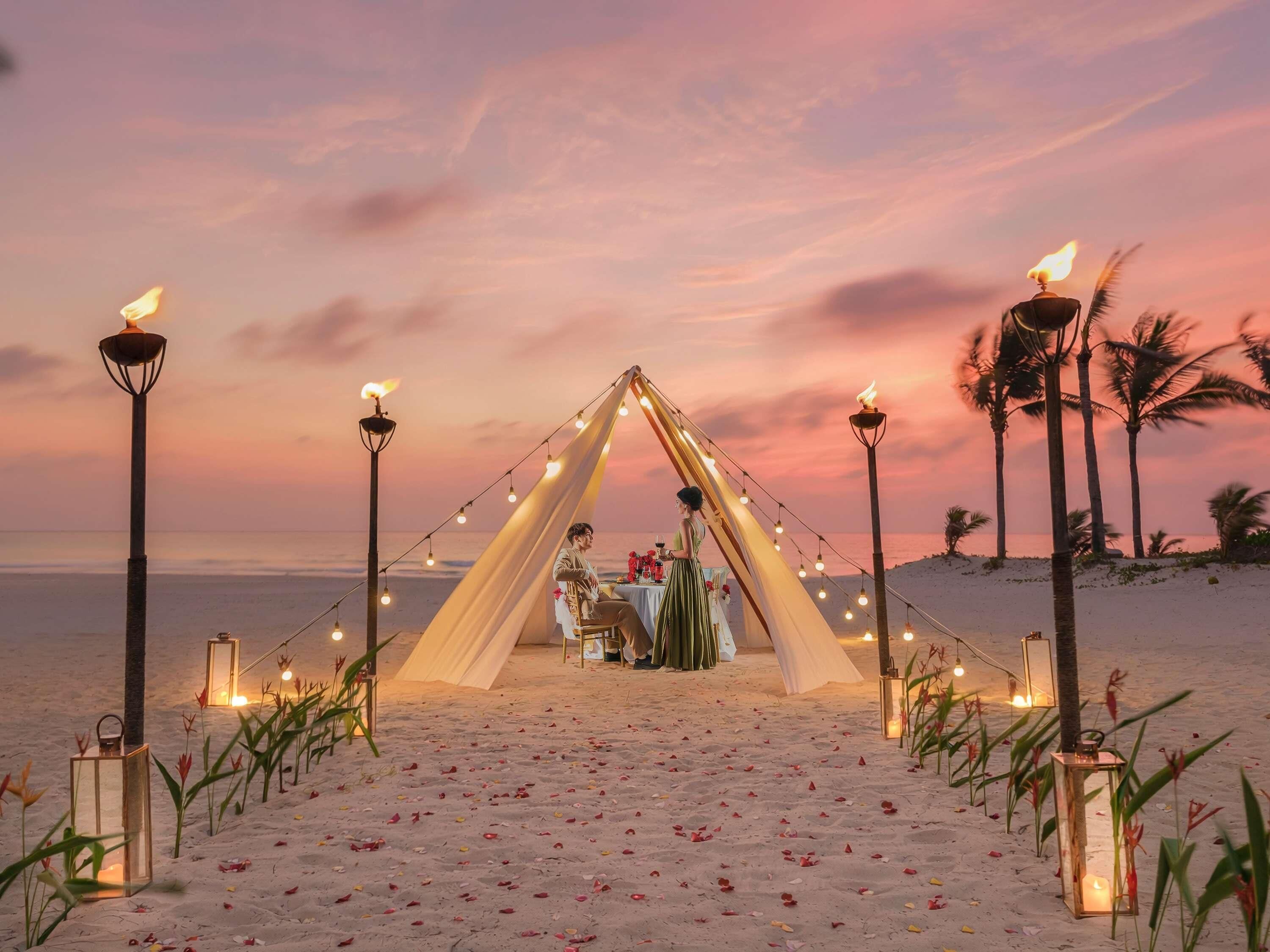A beach setting with a tented dining area, string lights, and lanterns.