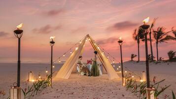 A beach setting with a tented dining area, string lights, and lanterns.