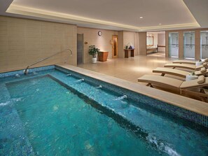A swimming pool with lounge chairs, a clock, and a plant.