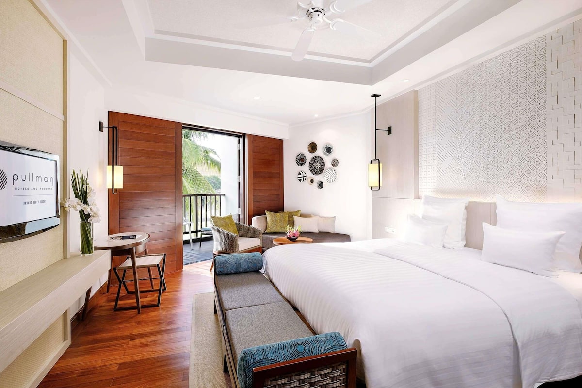 A hotel room with a bed, a seating area, a TV, and a balcony with a view.