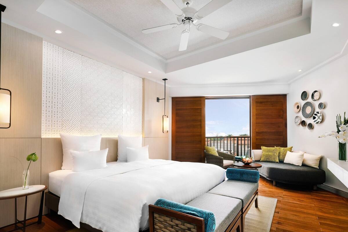 A modern bedroom with a large bed, a sofa, a balcony, and decorative wall art.