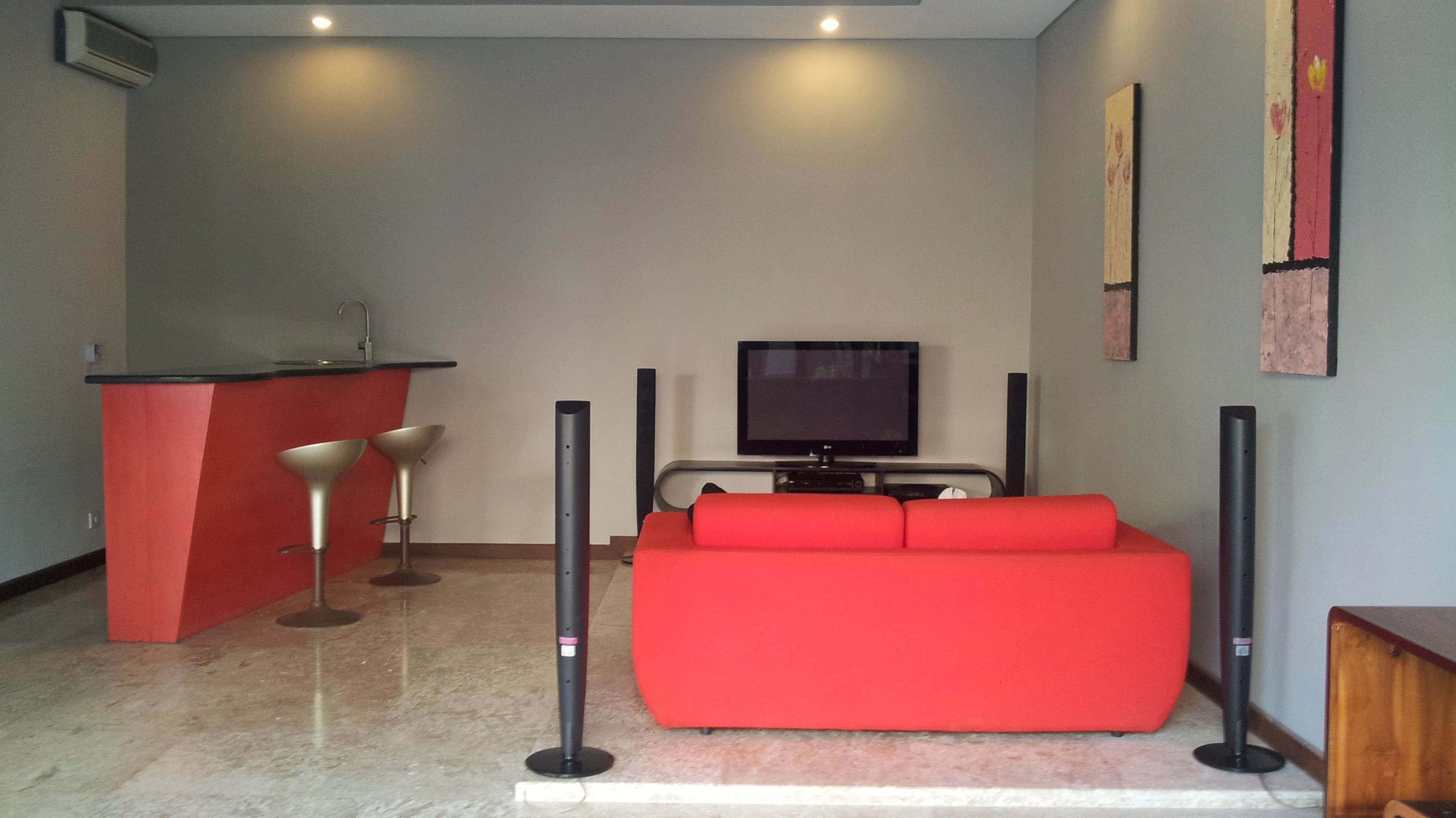 Un soggiorno con un divano rosso, una TV, un bancone bar rosso e due sgabelli da bar.