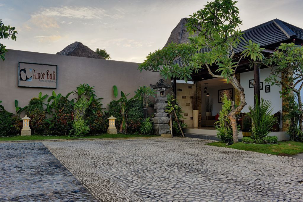 Entrada de hotel con un camino de adoquines que conduce a un edificio con un letrero que dice "Amor Bali".