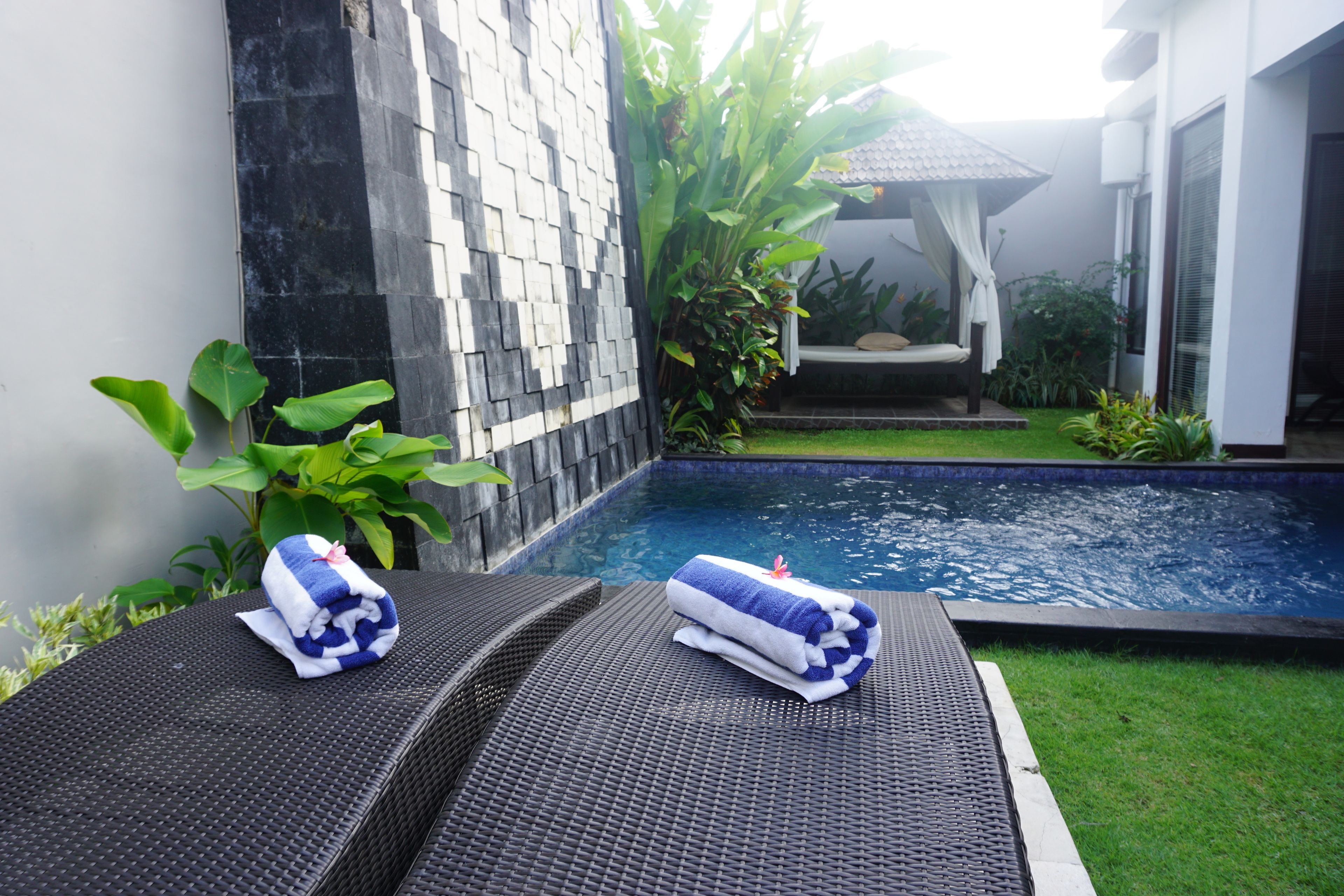 Zona junto a la piscina con dos tumbonas y toallas, rodeada de vegetación y un muro de azulejos.