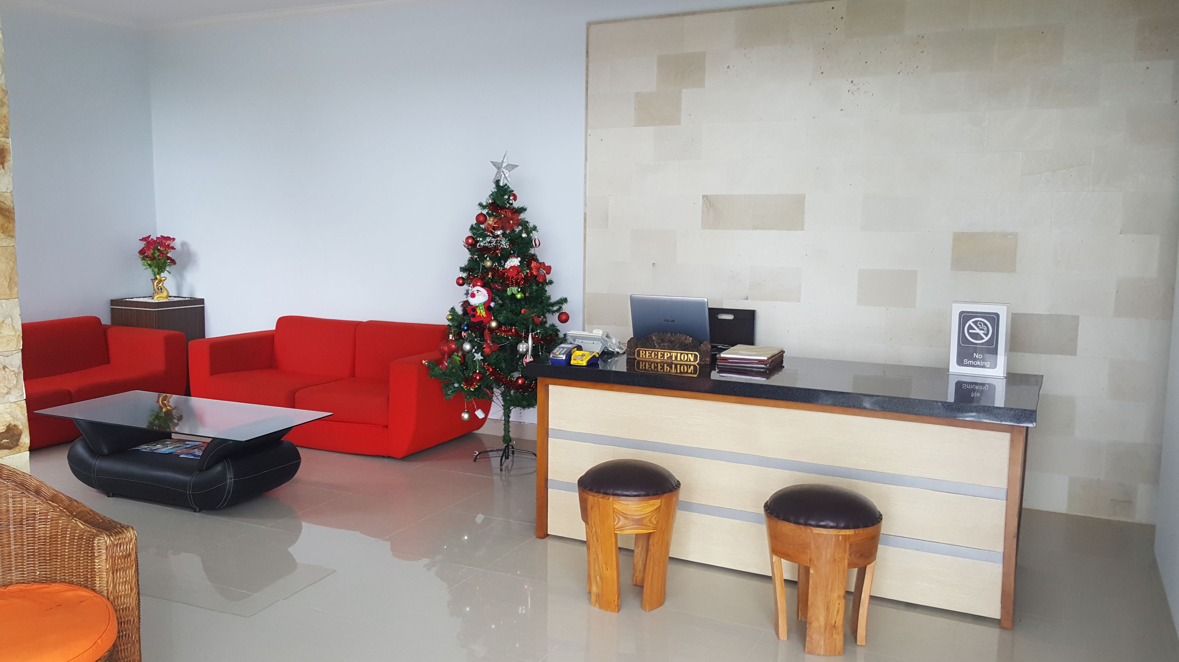 A reception area with a red sofa, a glass coffee table, a Christmas tree, a reception desk, and two wooden stools.