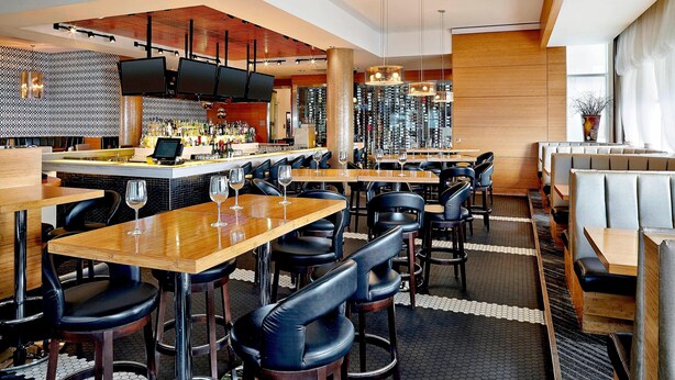 A modern restaurant with bar seating, high stools, and a central bar area. - Four Points by Sheraton Calgary Airport (Calgary)
