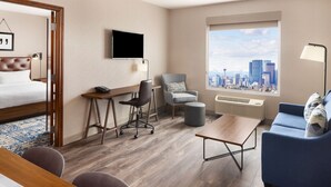 A hotel room with a bed, desk, chair, sofa, and a large window with a city view. - Four Points by Sheraton Calgary Airport (Calgary)