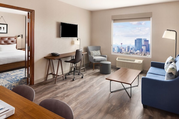 A hotel room with a bed, desk, chair, sofa, and a large window with a city view.