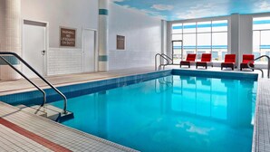An indoor swimming pool with clear blue water, red lounge chairs, and a view of the sky through large windows. - Four Points by Sheraton Calgary Airport (Calgary)
