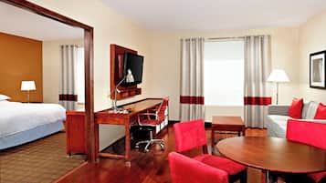 A hotel room with a bed, a desk with a computer, a TV, a dining table with chairs, and a sofa.