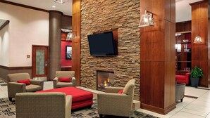 A lobby with a stone wall, a flat-screen TV, and a fireplace. There are several chairs and a red ottoman. - Four Points by Sheraton Calgary Airport (Calgary)