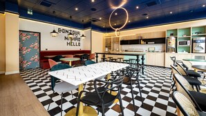 A restaurant with a checkered floor, a central table, and a kitchen area. - ibis styles Paris Gennevilliers (Gennevilliers)