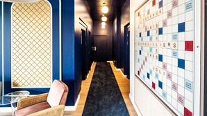 A hallway with a Scrabble board, a patterned wall, and a seating area with a chair and table. - ibis styles Paris Gennevilliers (Gennevilliers)