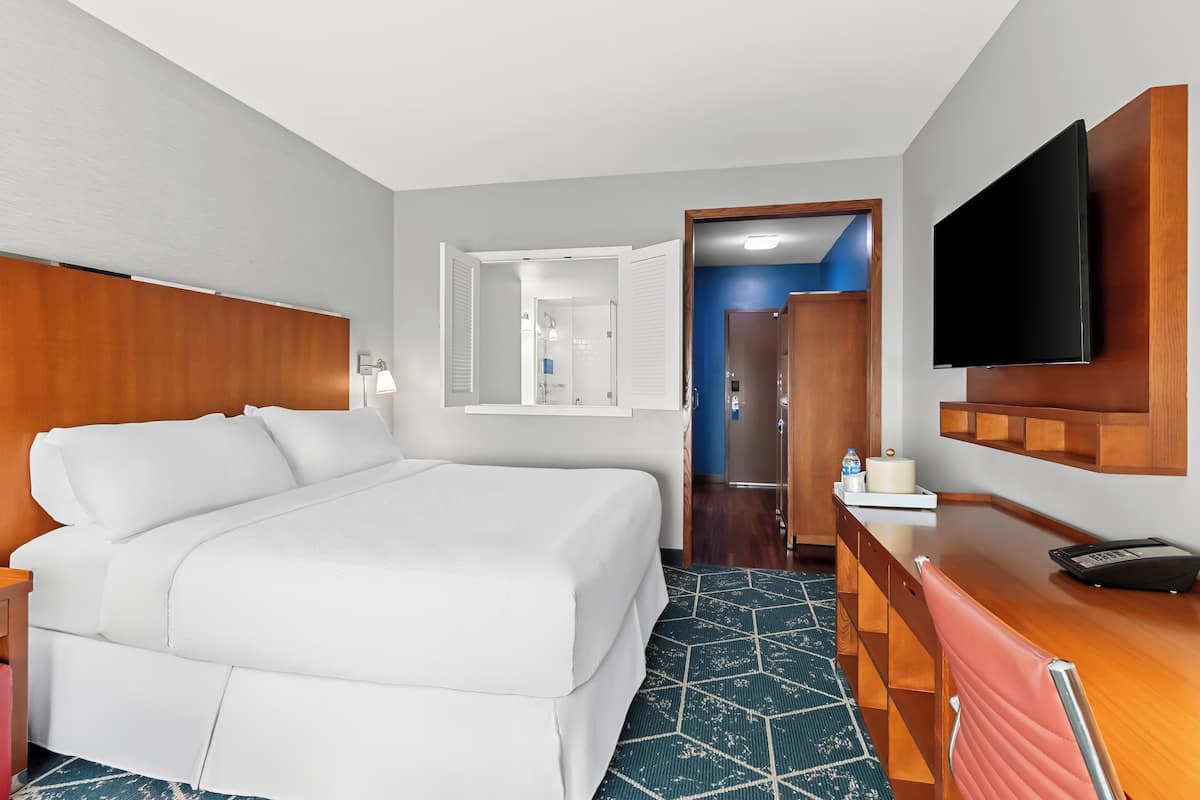 Ein Hotelzimmer mit Bett, Schreibtisch, Fernseher und einem durchgegangenen Tür sichtbaren Badezimmer.
