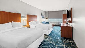 A hotel room with two beds, a desk, a chair, a TV, and a window.