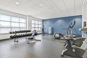 A gym with exercise equipment, a wall with a blue pattern, and windows providing natural light. - Four Points by Sheraton Oklahoma City Quail Springs (Oklahoma City)