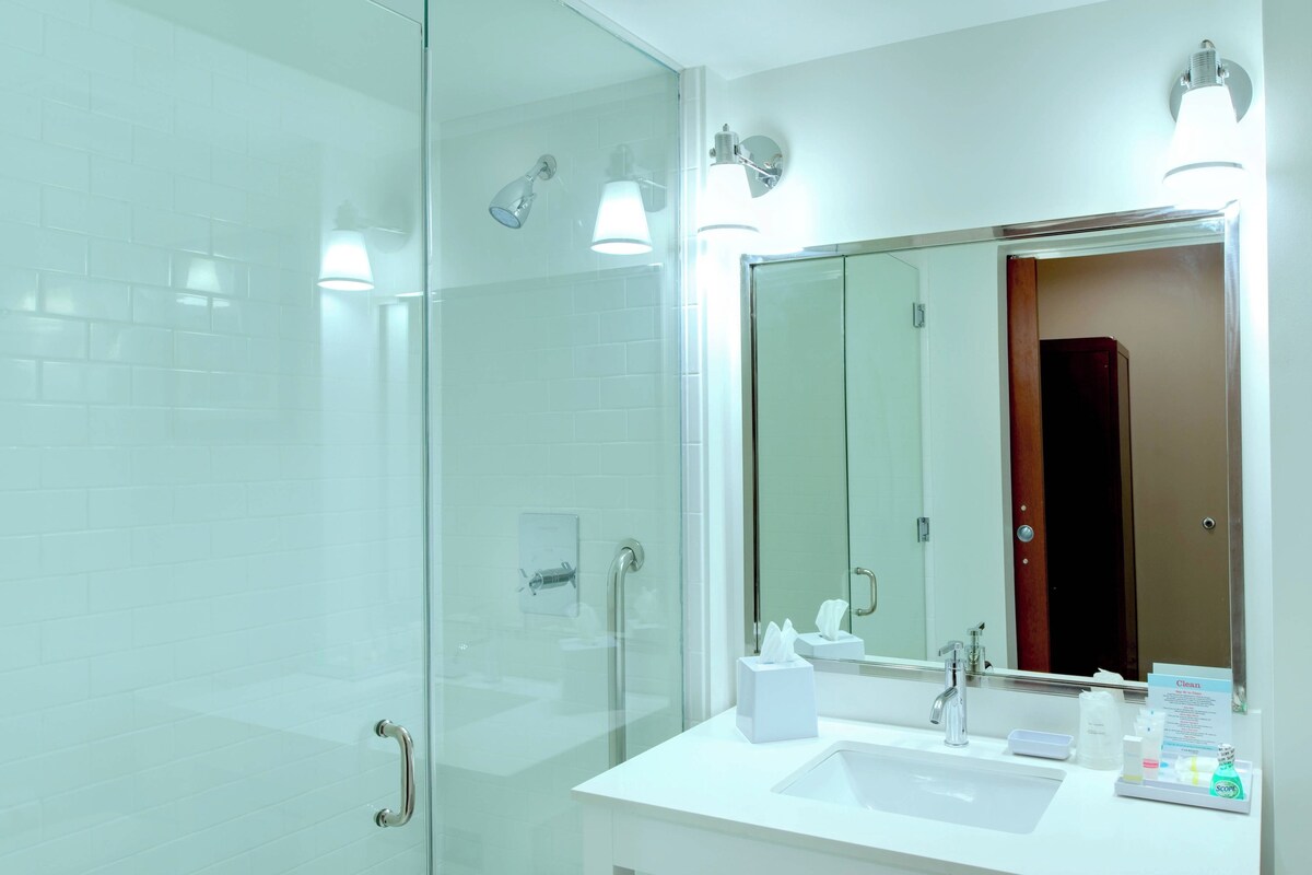 A modern bathroom with a glass shower enclosure, a white sink, and a large mirror with overhead lighting.