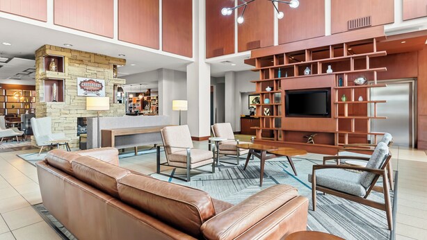 A spacious lobby with a leather sofa, armchairs, a coffee bar, and a TV.