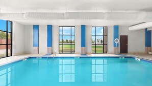 A modern indoor swimming pool with clear windows, a door, and a visible exit sign.