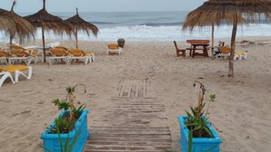 Ein Strand mit Reetdachsonnenstühlen, Liegestühlen und einem Holzsteg, der zum Meer führt.