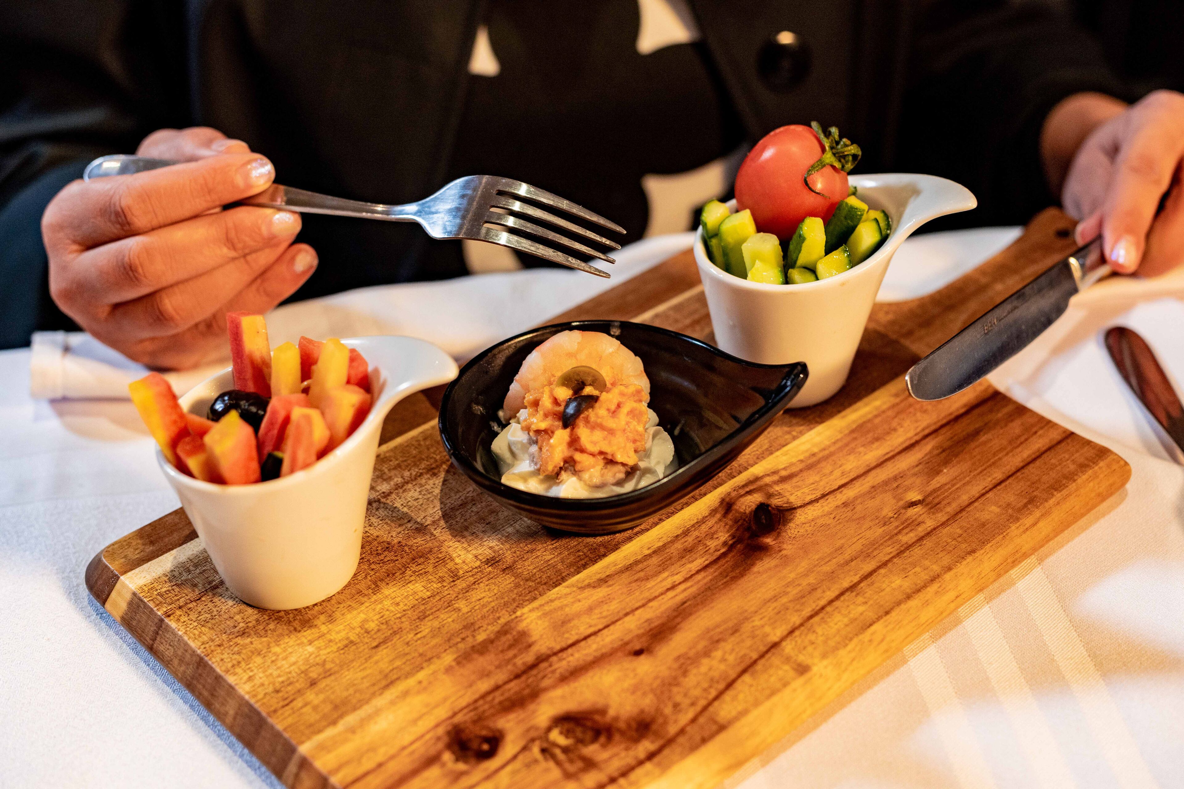 Une planche en bois sur laquelle sont disposés trois bols contenant différents aliments : un bol de fruits coupés, un bol de plat de fruits de mer et un bol de salade de légumes.