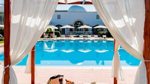 Ein Poolbereich mit freiem Blick auf den Pool, Liegestühle, Sonnenschirme und ein Gebäude im Hintergrund.