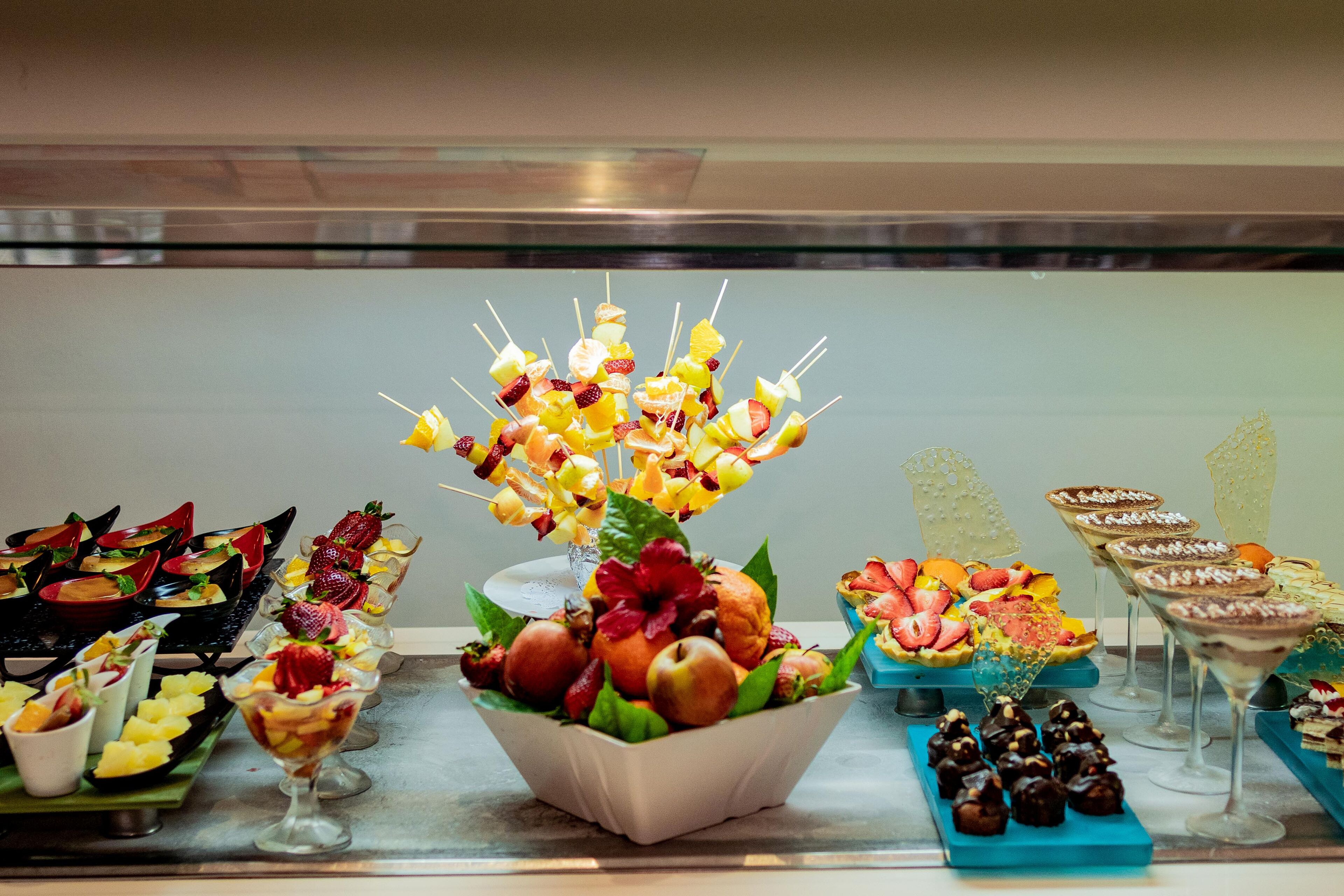 A buffet with various food items including fruit skewers, desserts, and appetizers.