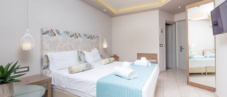 A modern hotel room with a large bed, bedside tables, a potted plant, and a TV.