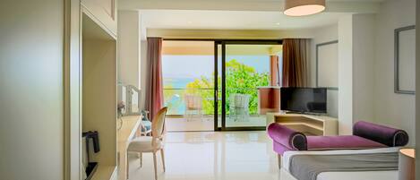A modern hotel room with a bed, a desk, a TV, and a balcony with a view of the sea.