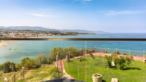 Vista costeira com área gramada, caminho pavimentado e cerca com vista para o mar.
