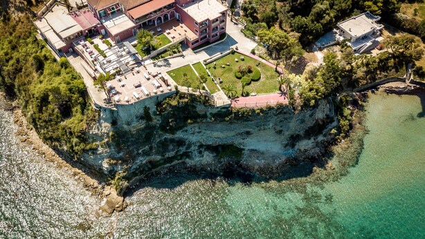 Vista aérea de uma propriedade costeira com um edifício grande, uma piscina e um penhasco com vista para o mar.
