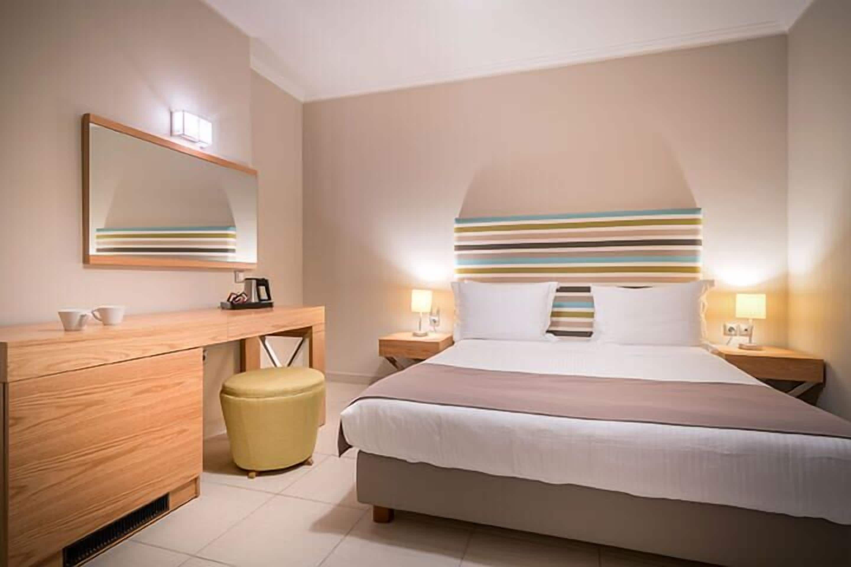 A modern hotel room with a large bed, a wooden desk, a mirror, and two bedside lamps.