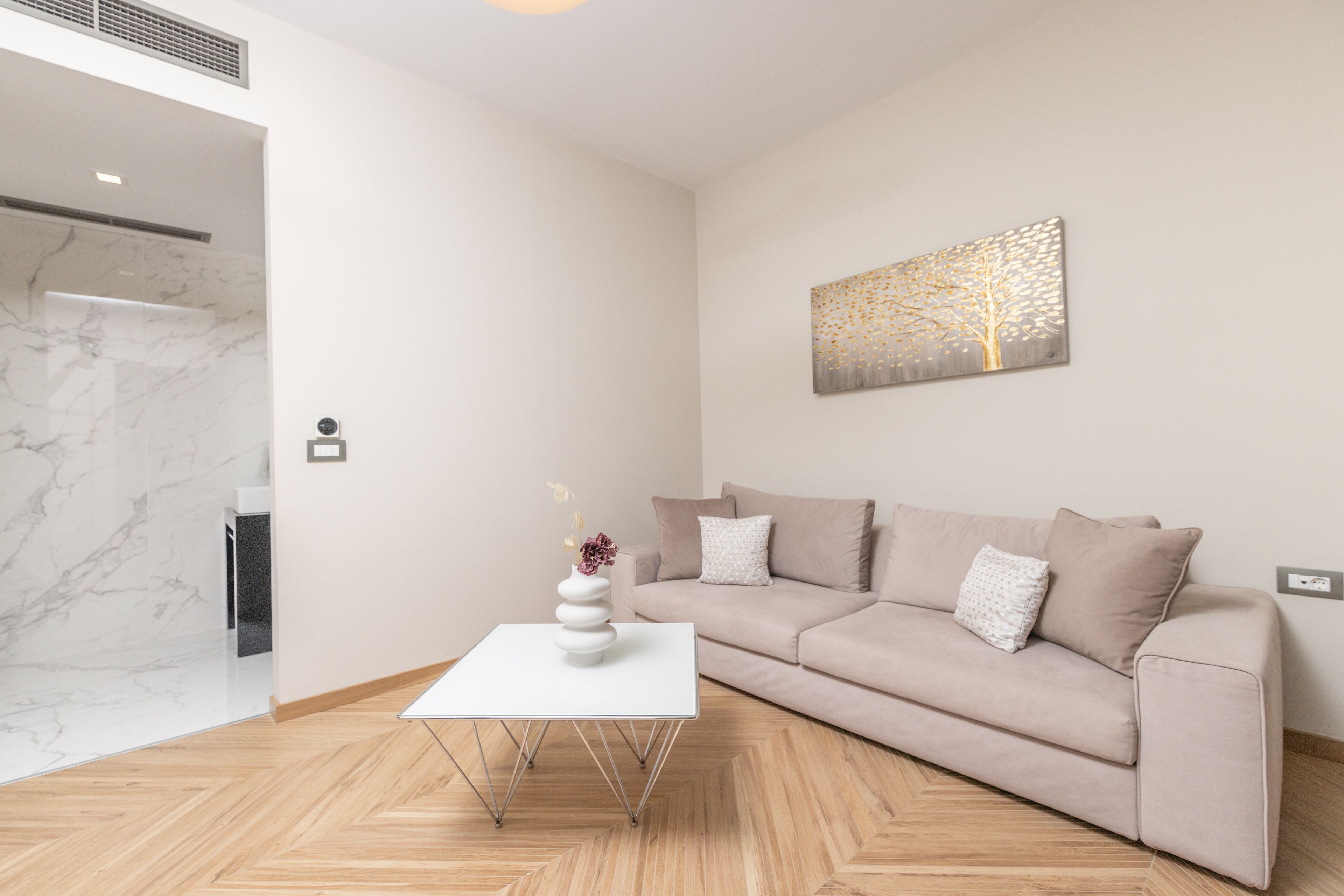 A modern living room with a marble floor, a white coffee table, a beige sofa, and a wall-mounted artwork.