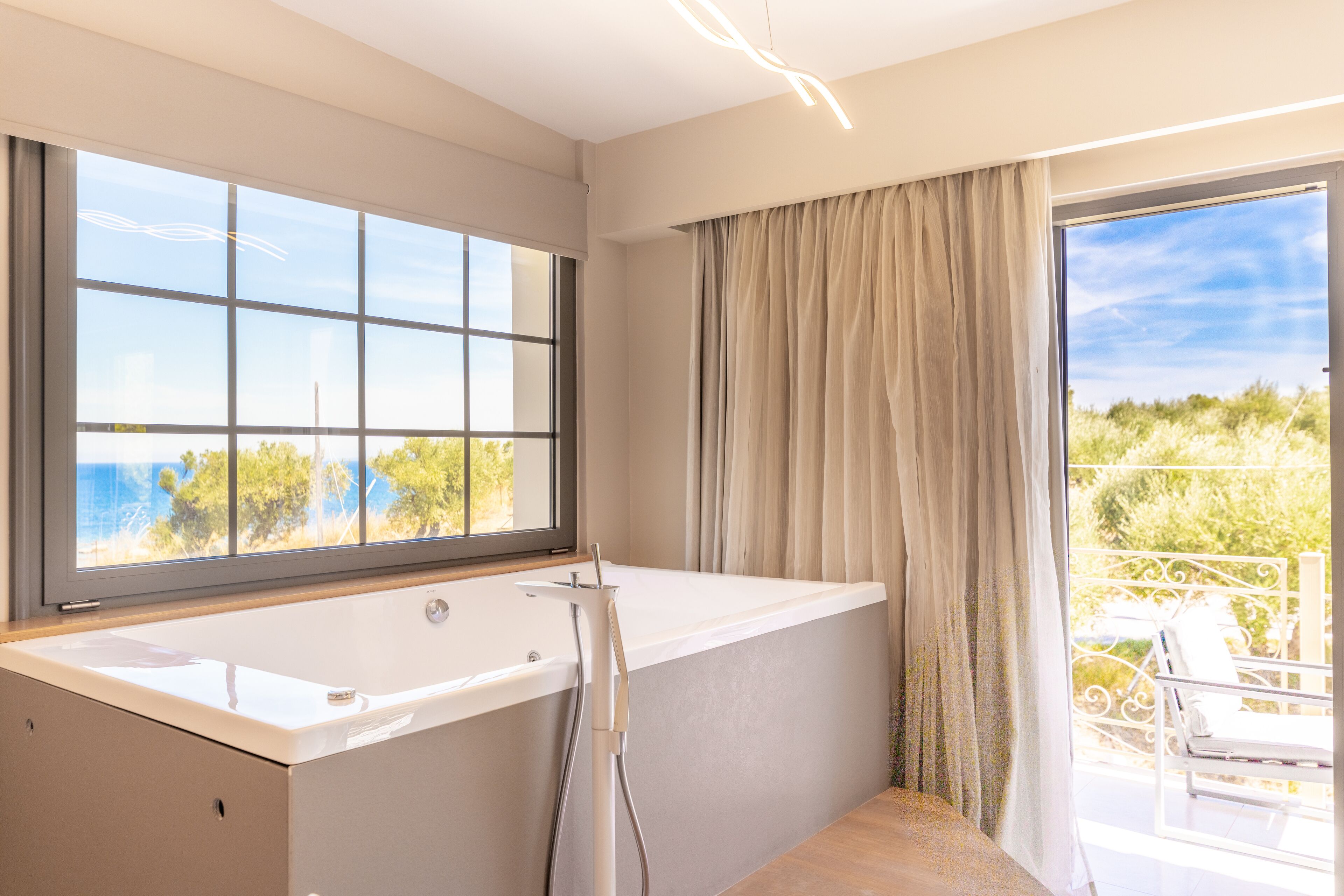 Un baño moderno con una bañera grande, una ventana con vista al mar y un balcón con mobiliario exterior.