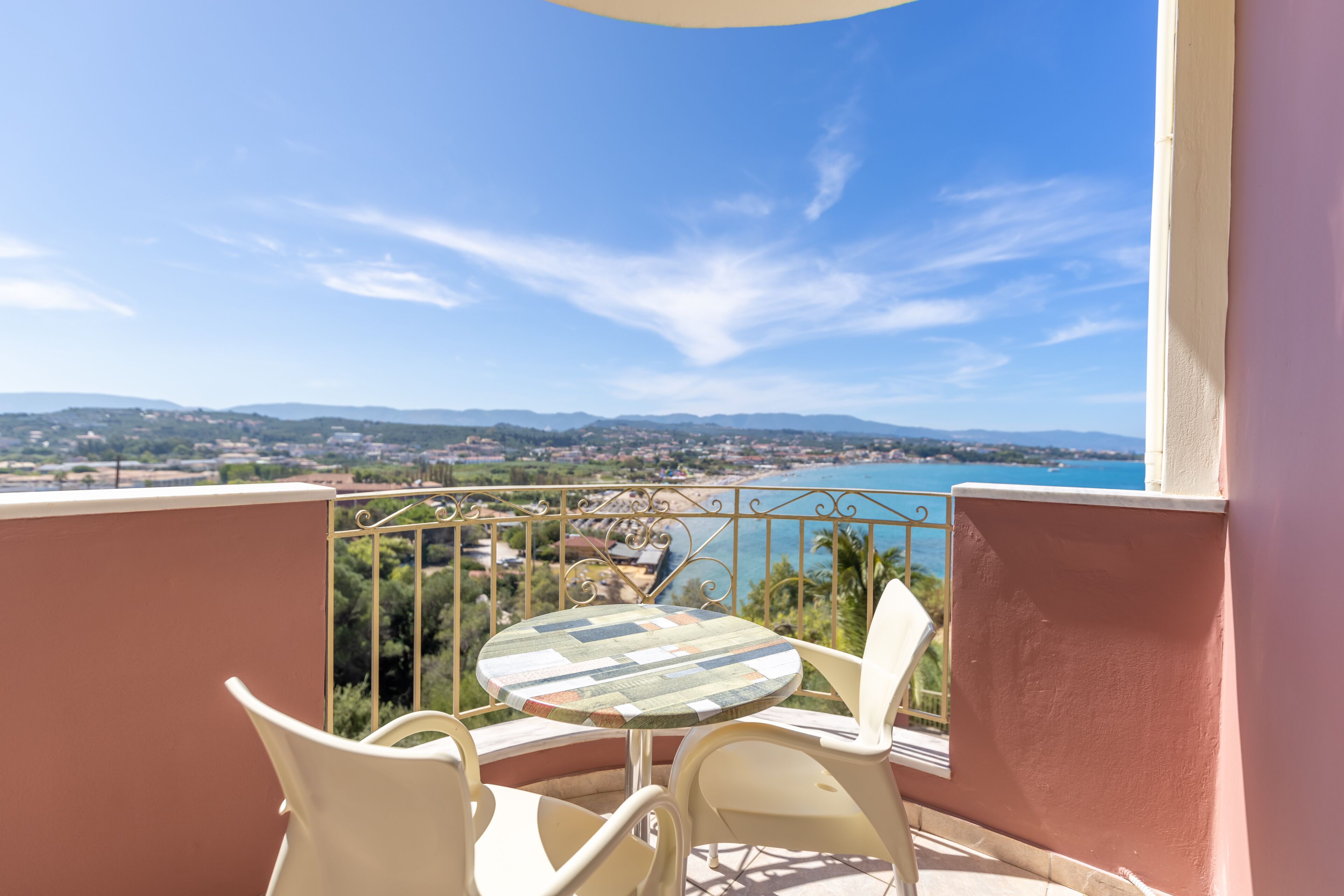 Un balcon avec une table et des chaises, offrant une vue panoramique sur une ville côtière et une étendue d’eau.