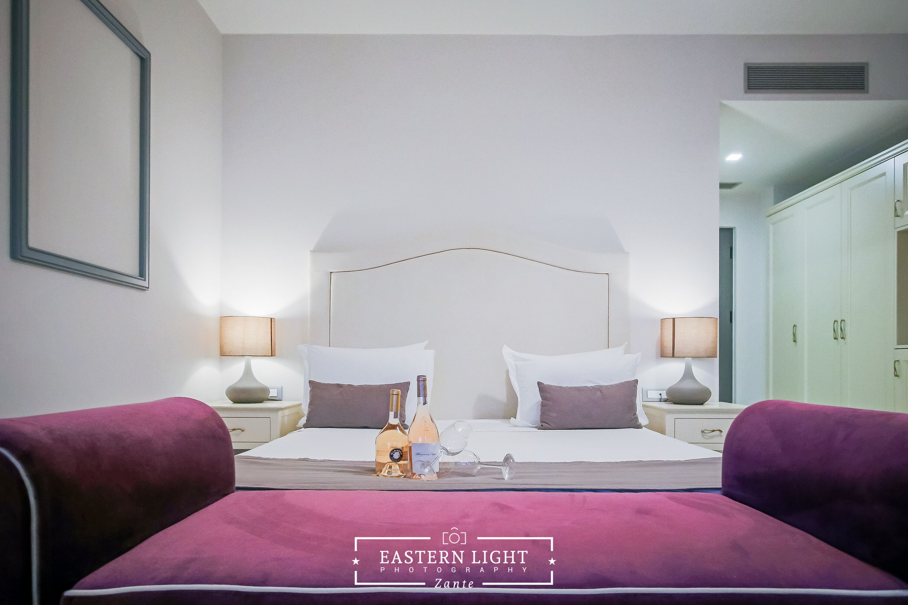 A hotel room with a large bed, two bedside tables, a wardrobe, and a framed picture on the wall.