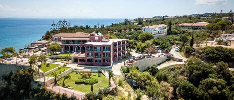 A coastal property with a large building, landscaped gardens, and a view of the sea.