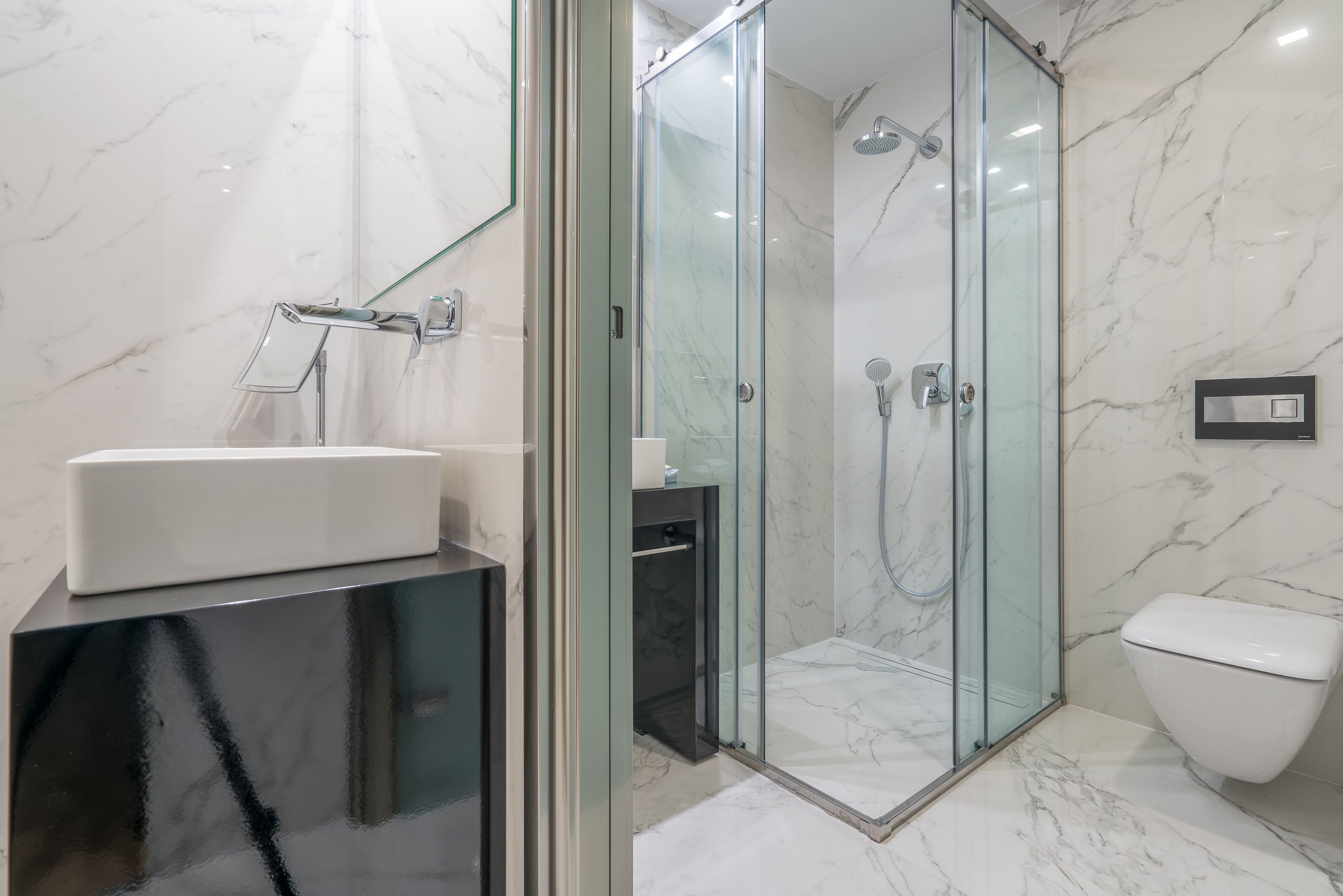 Un bany modern amb dutxa de vidre, un lavabo blanc i un vàter.