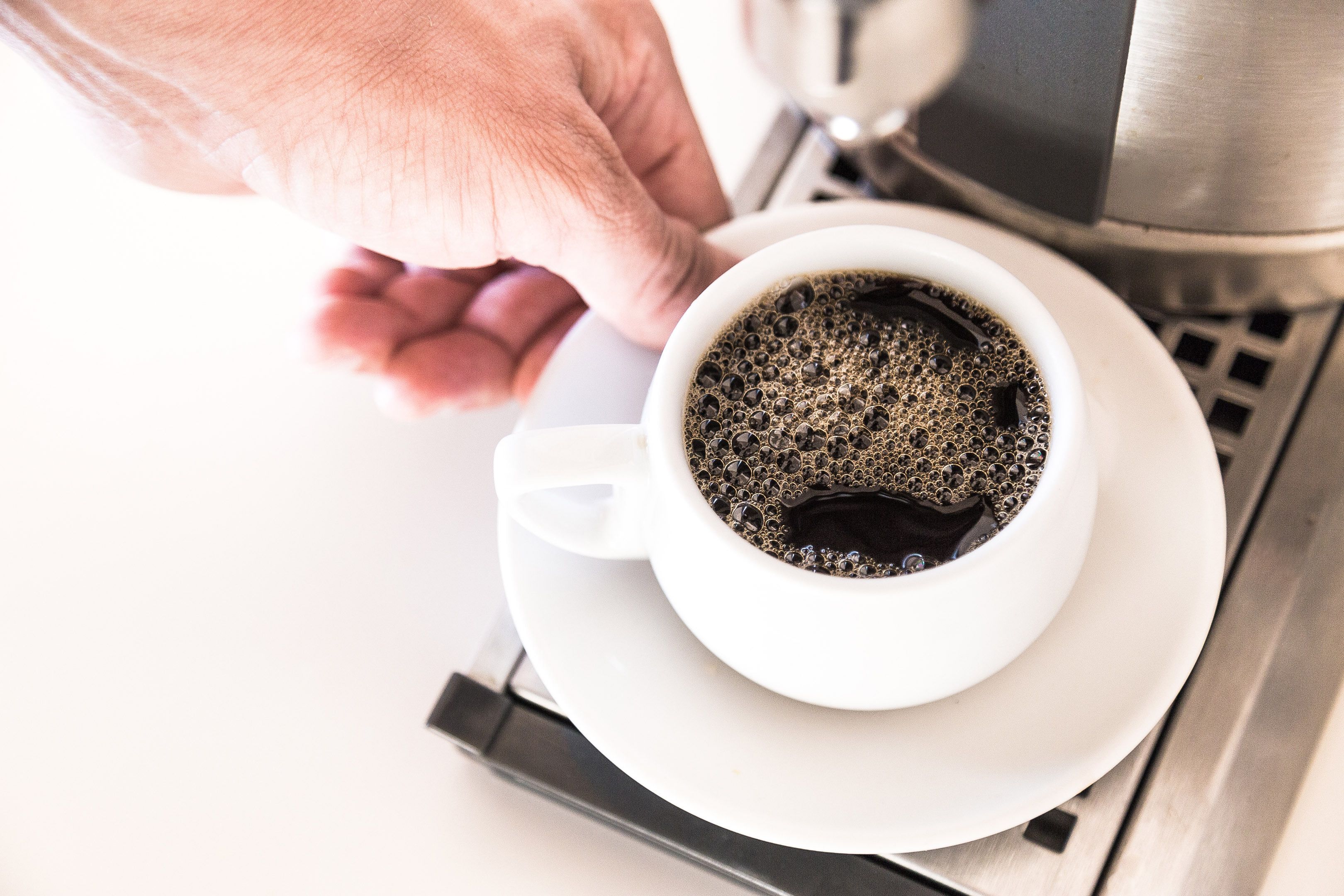 Una tassa de cafè sobre un calze al costat d'una cafetera.